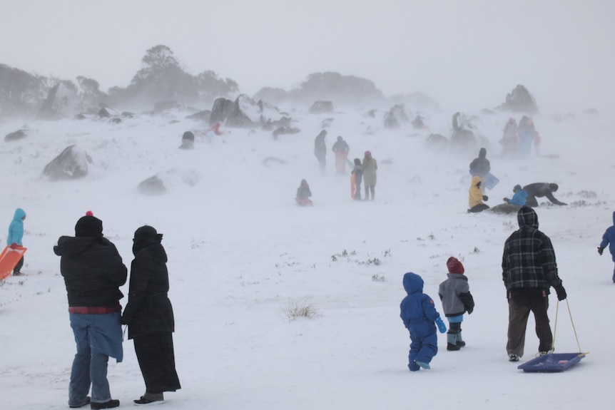 Snowy hazy day with people dressed in snow gear dragging toboggans.