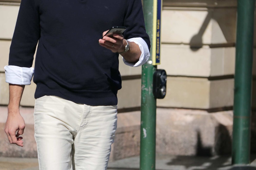 A man holds a mobile phone while waiting to cross the road in Brisbane's CBD.