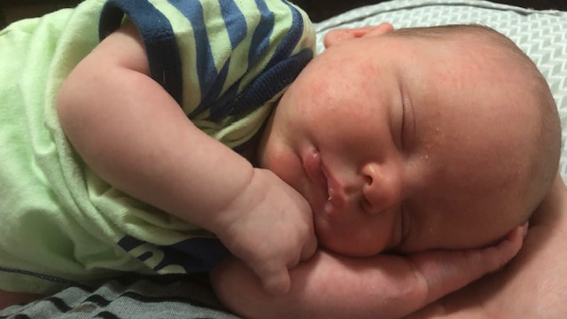 A close up image of a baby sleeping, his eyes are closed and he is lying on one arm.