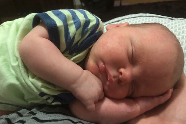 A close up image of a baby sleeping, his eyes are closed and he is lying on one arm.