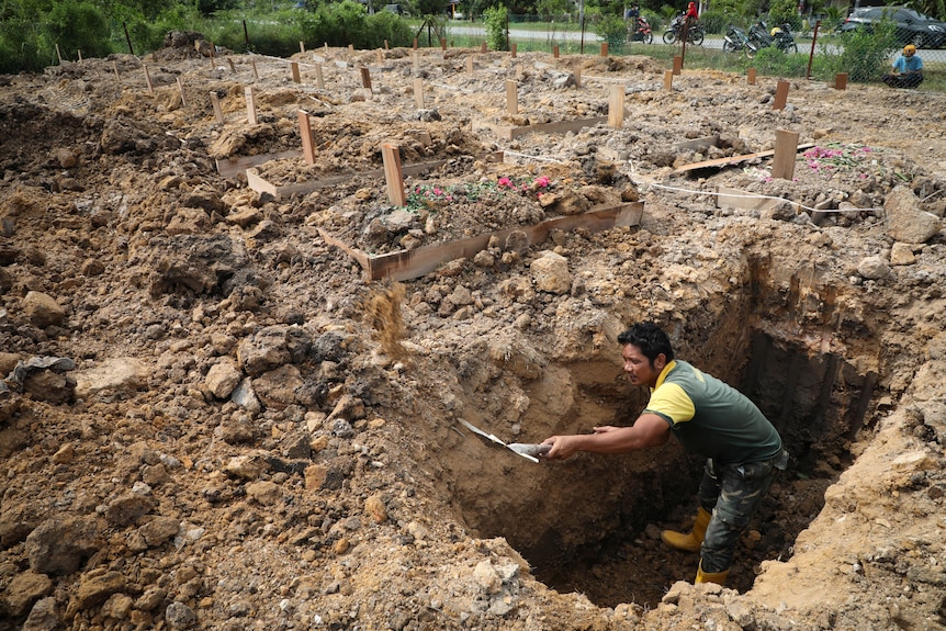 A cemetary worker digs a grave for a COVID-19 victim in a graveyard crowded with fresh graves from the pandemic.