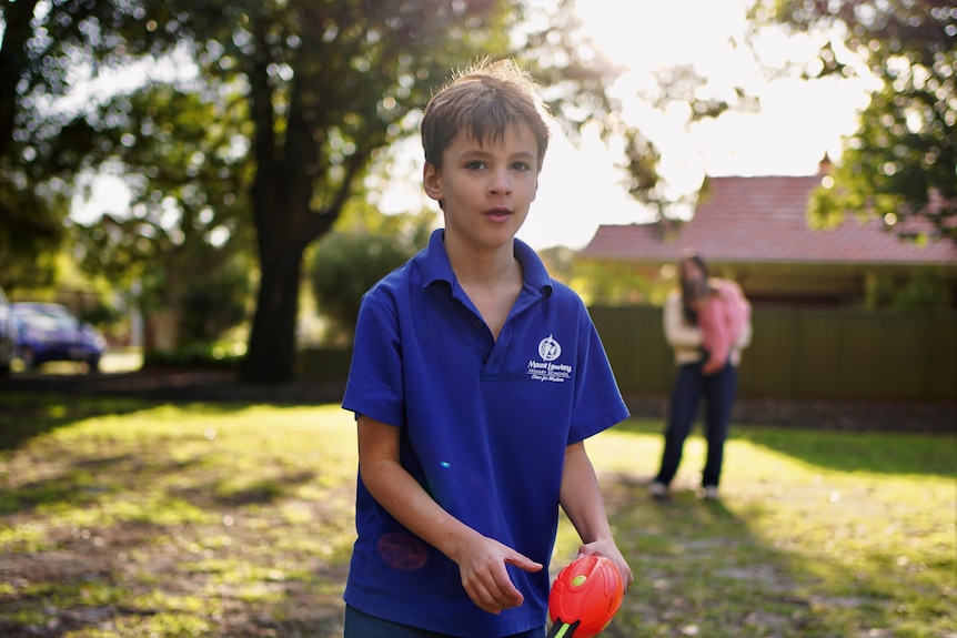 A young white boy in a blue school uniform, playing in a park