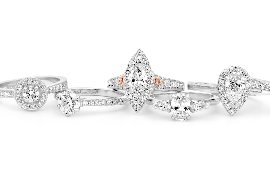 Six diamond rings with different shaped stones sitting side by side.