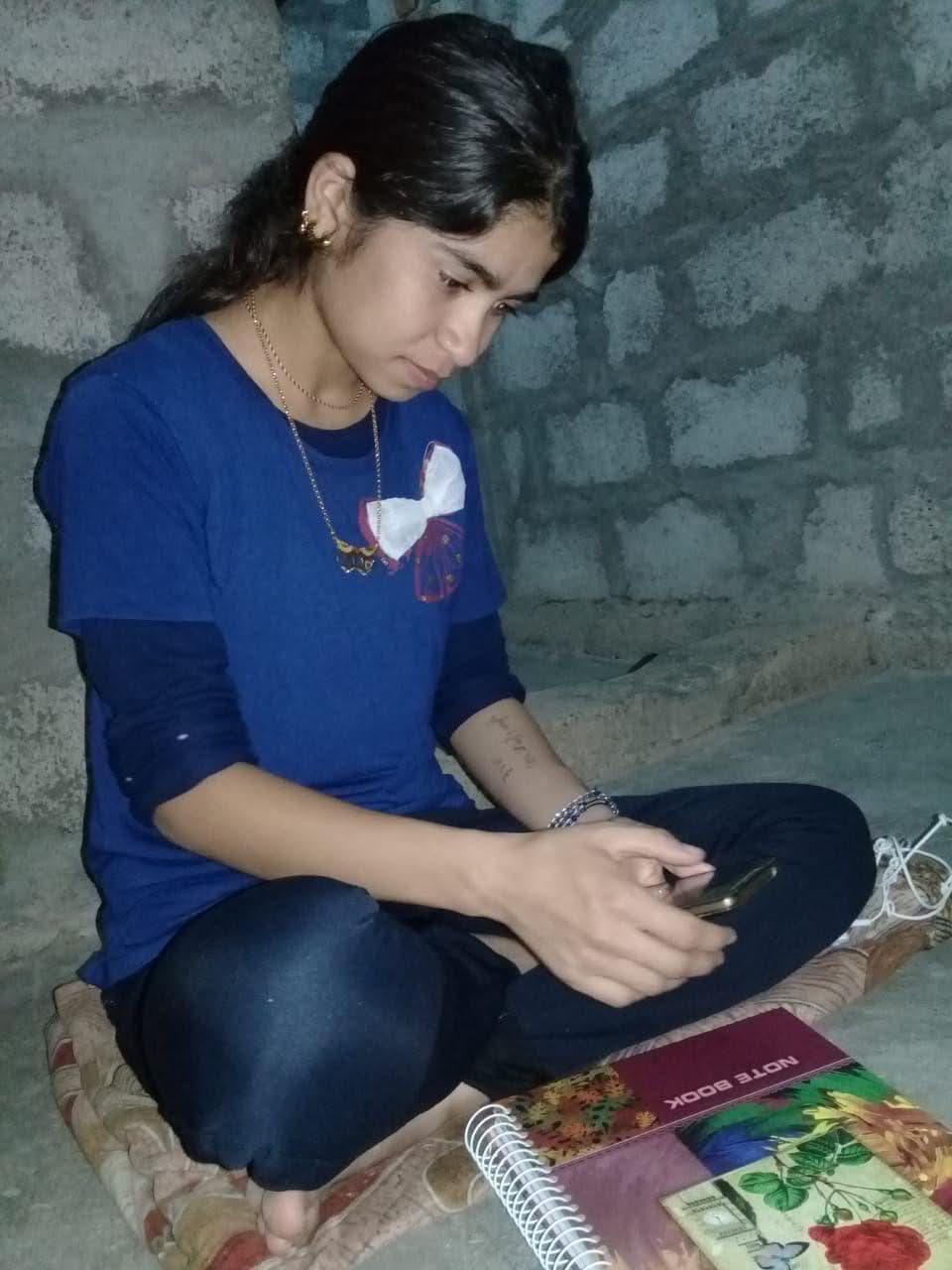 Young woman in blue top sits on the ground looking down.