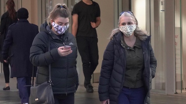 Two women wear patterned face masks while walking on a city street in winter clothes