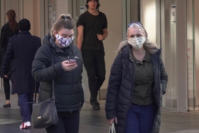 Two women wear patterned face masks while walking on a city street in winter clothes