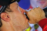 Sebastian Vettel leans back and drinks from an over-sized champagne magnum as Charles Leclerc looks downcast in the background