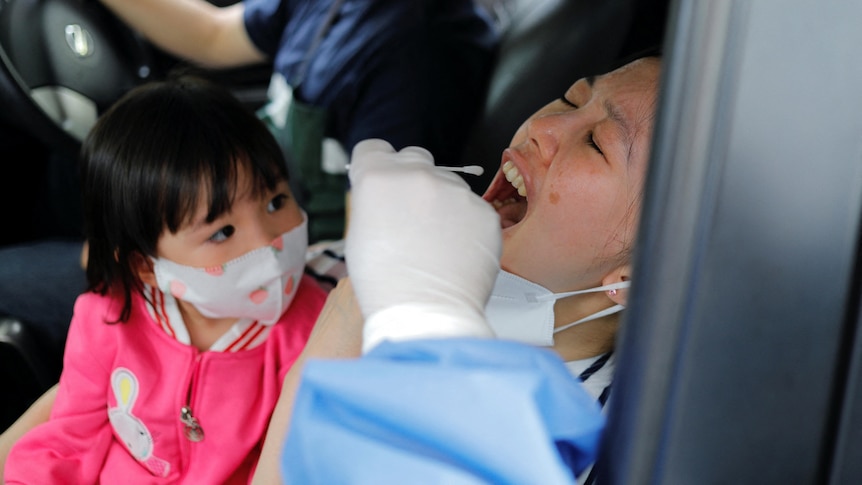A woman reacts as a medical worker takes her swab sample at a drive-thru centre.
