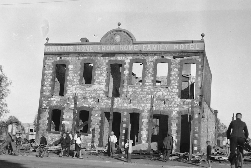 A black and white photo of a damaged hotel building as people walk by