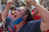 A woman shouting with her mask on her chin and her fists in the air.
