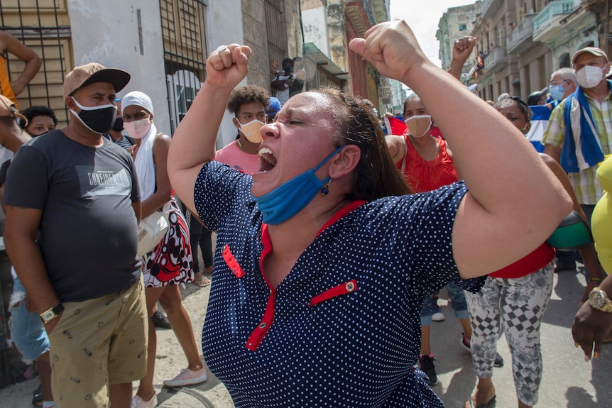 A woman shouting with her mask on her chin and her fists in the air.