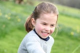 Princess Charlotte runs outdoors holding a flower and smiling