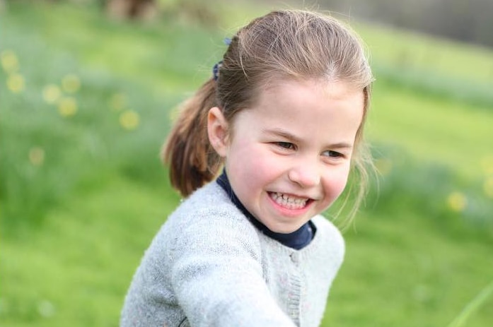 Princess Charlotte runs outdoors holding a flower and smiling