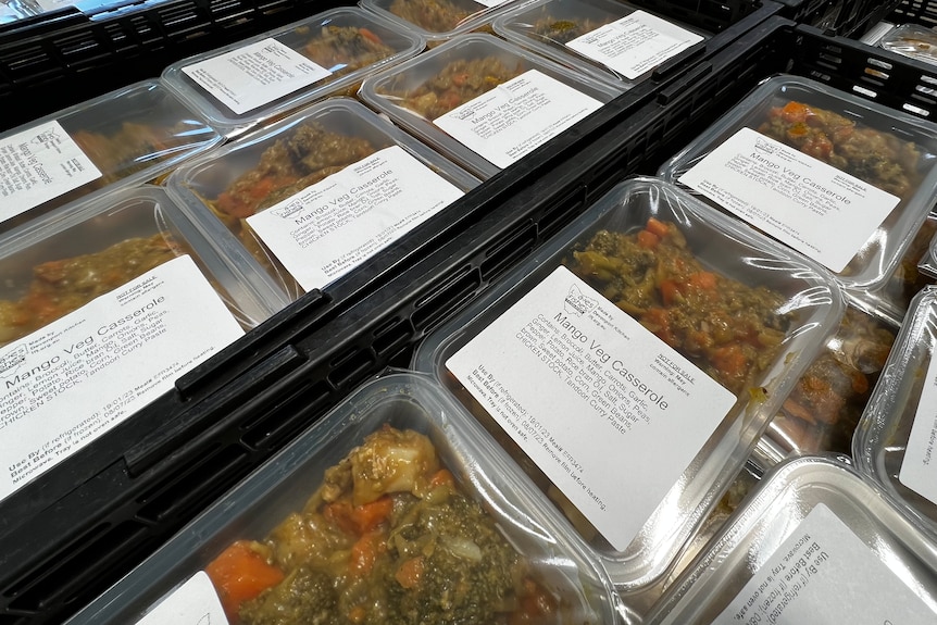 Crates of pre-prepared meals in plastic containers sit in a large warehouse.