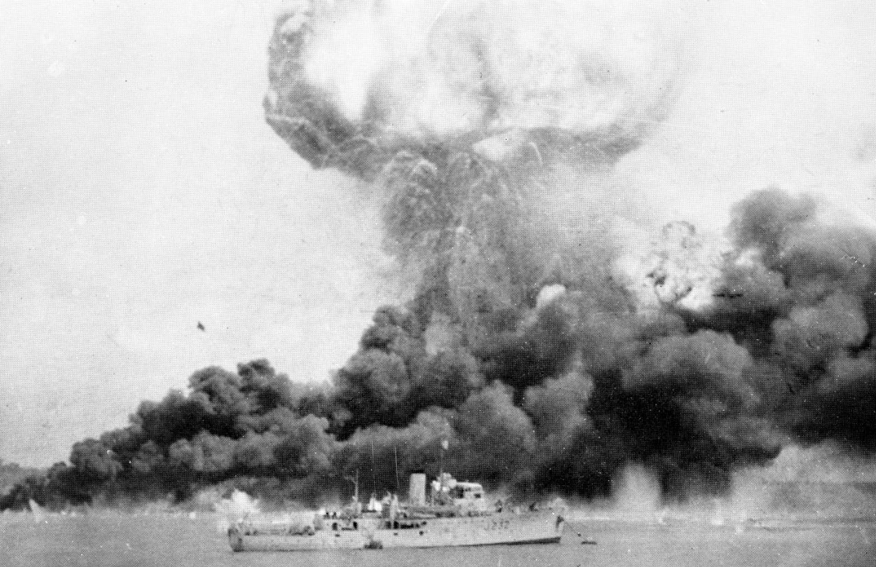Dense clouds of smoke rise from oil tanks hit during the first Japanese air raid.