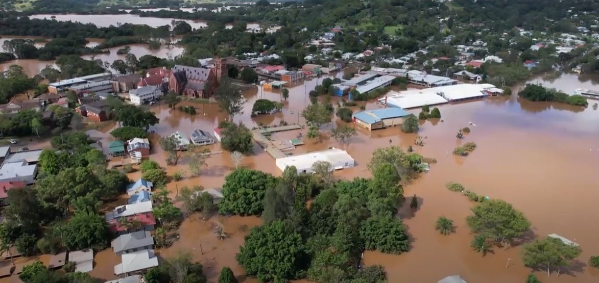 Aerial picture shows roofs of buildings above brown flood water.