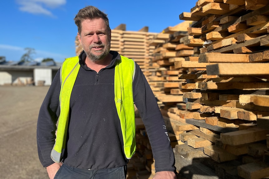 A man in hi vis stands in front of a stack of timber