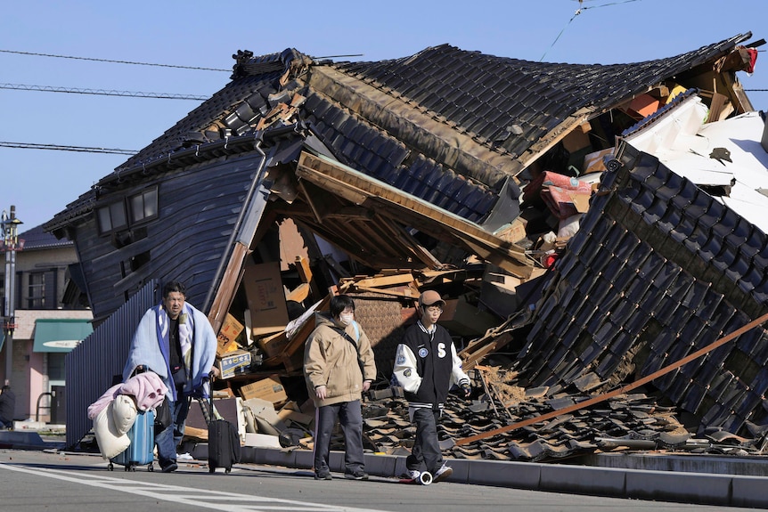 People walk past a house that has been damaged by an earthquake.