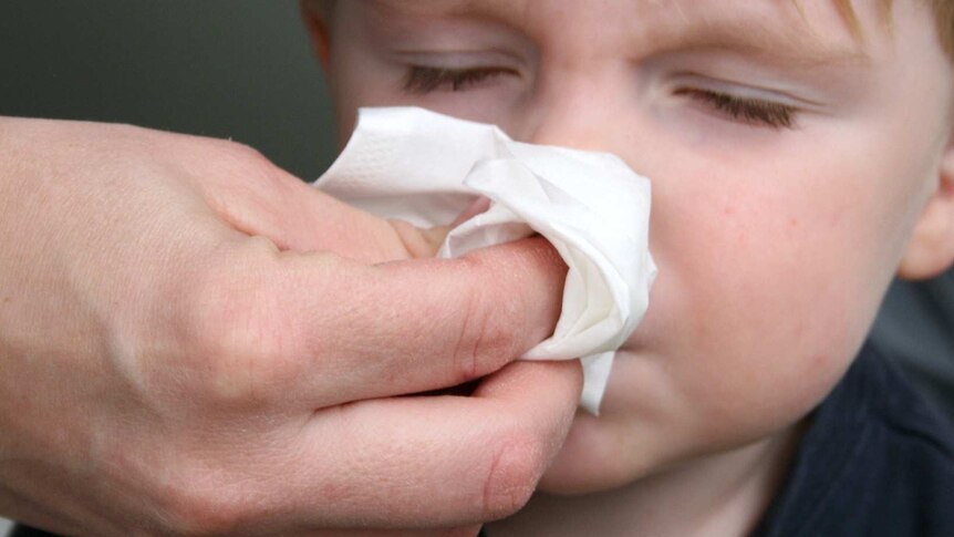 A parent helps a small boy blow his nose.