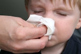 A parent helps a small boy blow his nose.