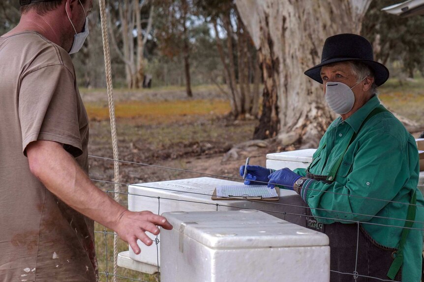 a woman holding a notepad and wearing a mask talks with a customer at an outside farmgate vegetable collection