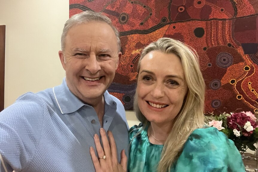 Anthony Albanese, in a blue polo shirt, standing with his wife with her left hand on his chest, showing an engagement ring.