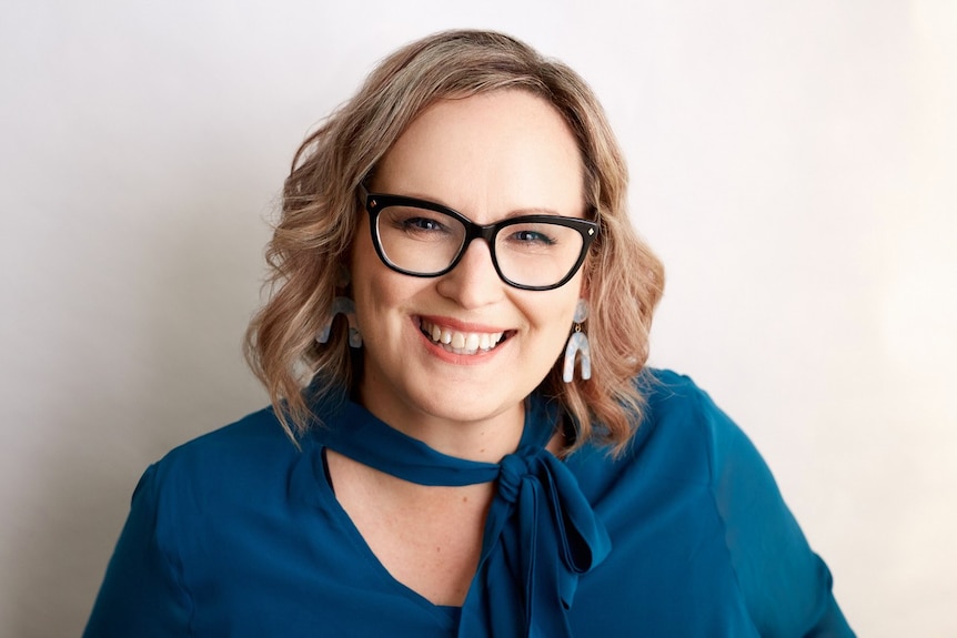 Emma Heuston, wearing dark spectacles and a teal top, poses for a photo