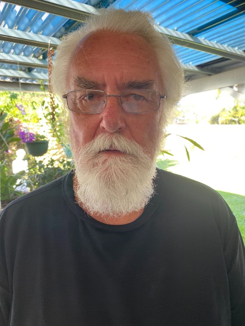 An older man with white hair, glasses and a beard wears a black t shirt