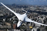 A white plane flies over a city 