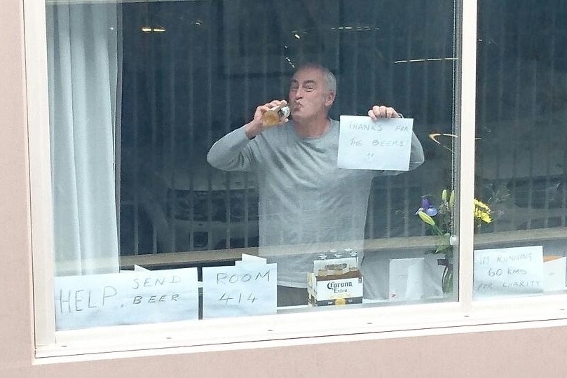 A man drinking beer behind a window showing a sign on paper