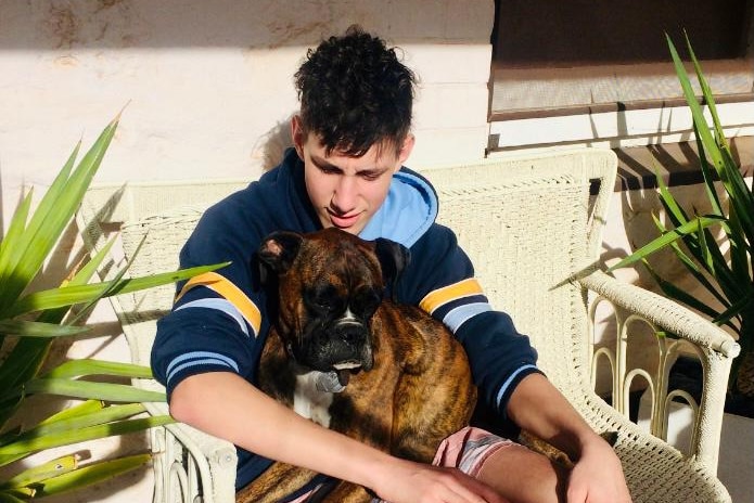 A high school student sits down with a dog on his lap.