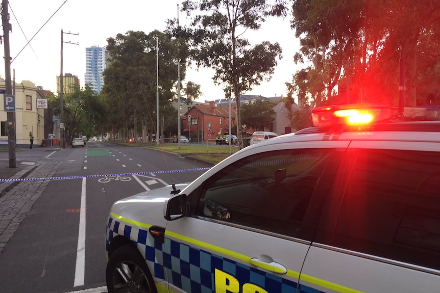 A police car sits on the road in front of police tape.