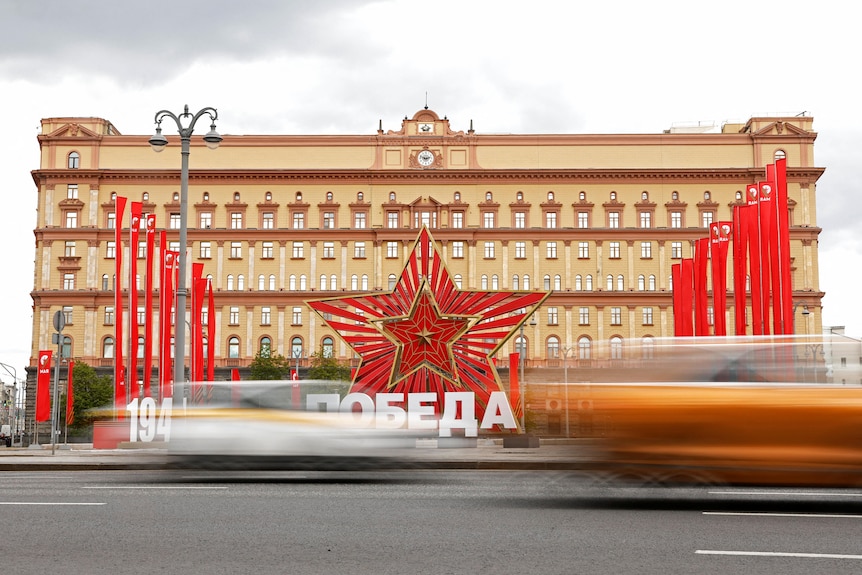 Traffic blurs in front of large building with red star decoration and red banners. 