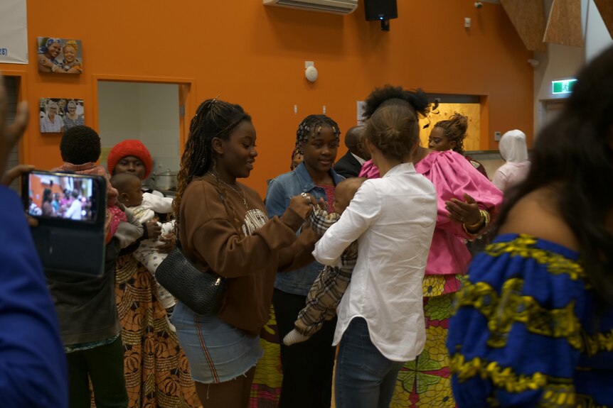 A Congolese teenage girl wearing a blue jumper and smiling at the female host. 