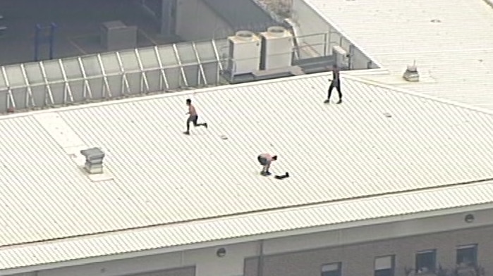 three people atop a building roof, two of them shirtless