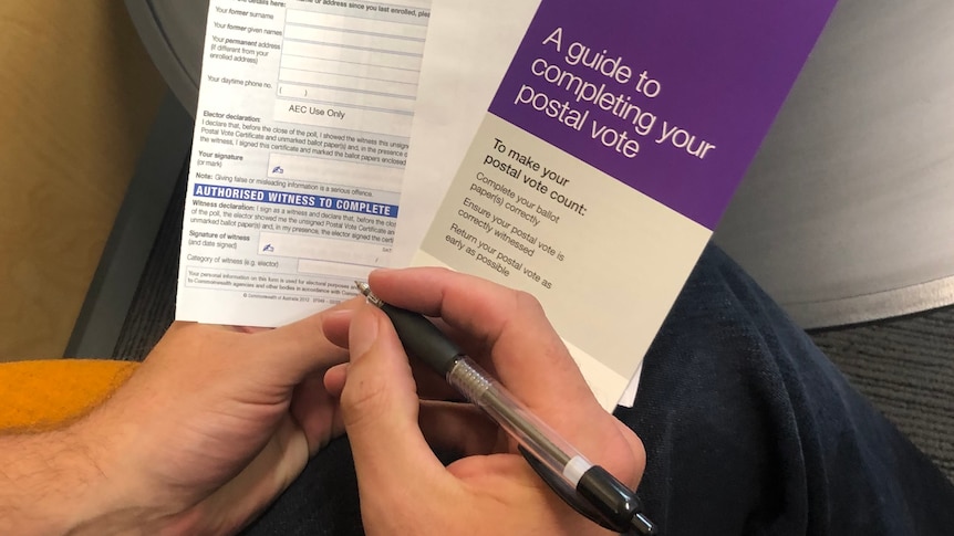 A person holds a pen and a stack of postal vote papers. 