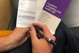 A person holds a pen and a stack of postal vote papers. 