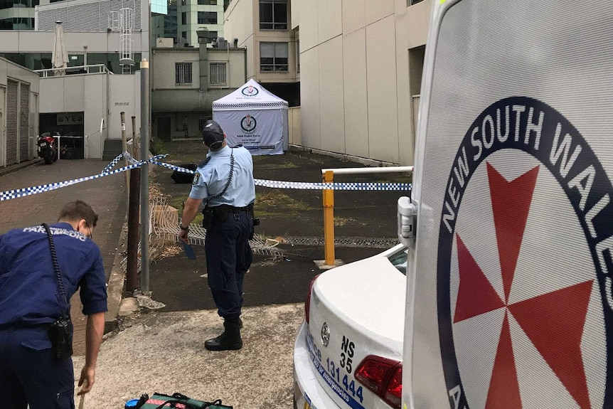 Police looking up near a white-tented area cordoned off by police.