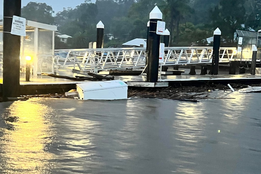 A fridge and wooden debris washes up against a ferry wharf.