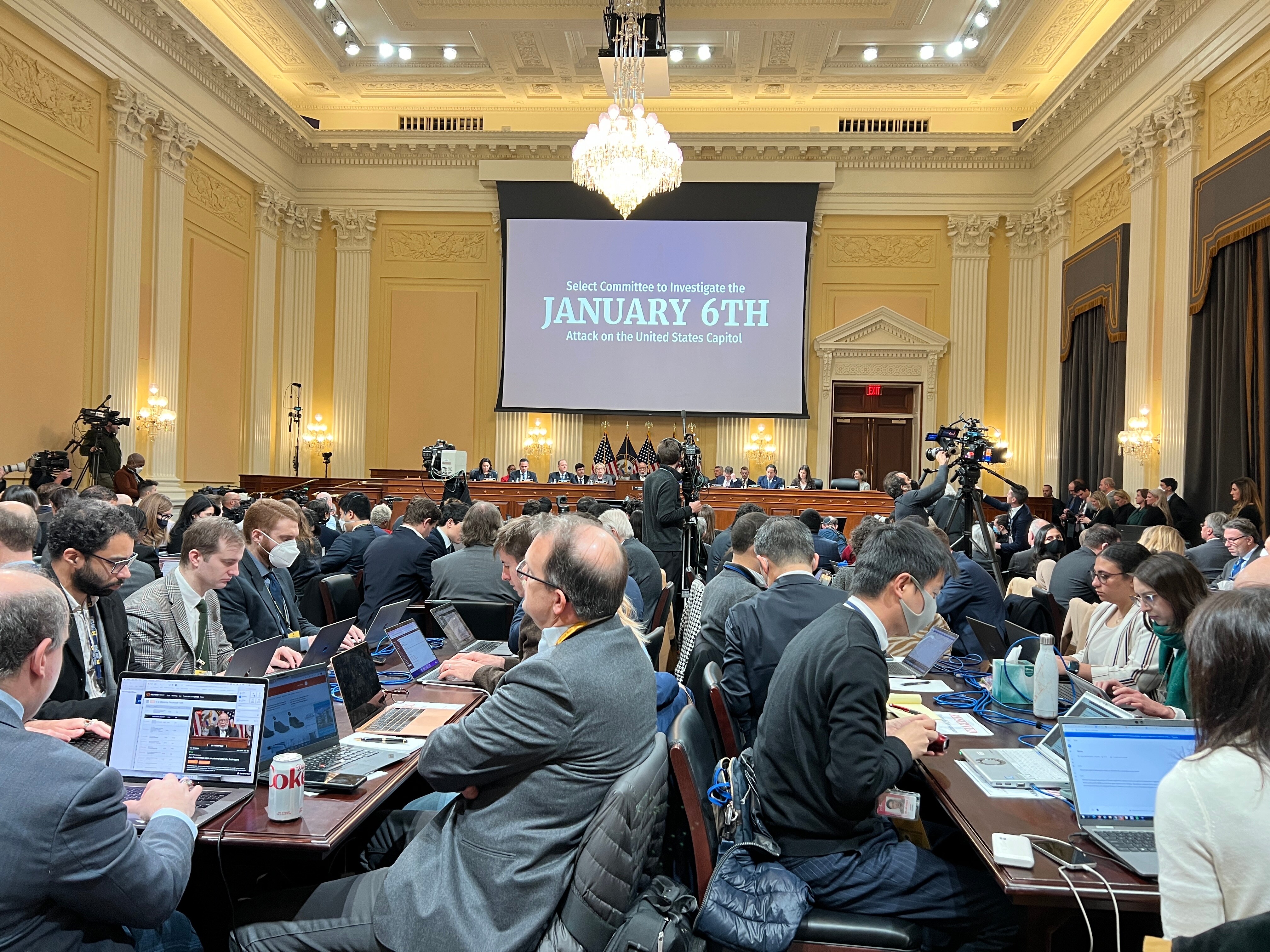 A group of people, some wearing masks, sit at desks pouring over documents in a big room.