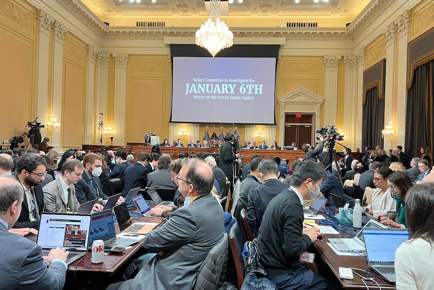 A group of people, some wearing masks, sit at desks pouring over documents in a big room.