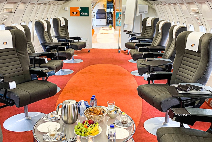 Plush conference room in a plane fuselage with bright orange carpets and refreshments on table.