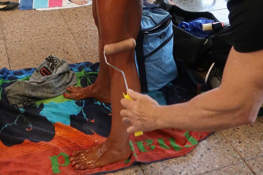 A contestant gets help applying fake tan to her legs with a roller.