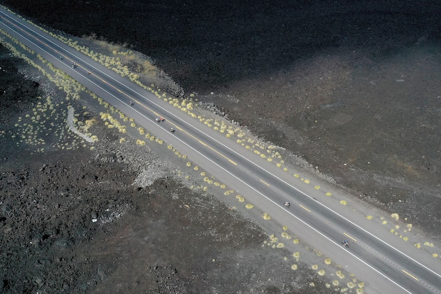 Cyclists ride on a road with black ground on either side