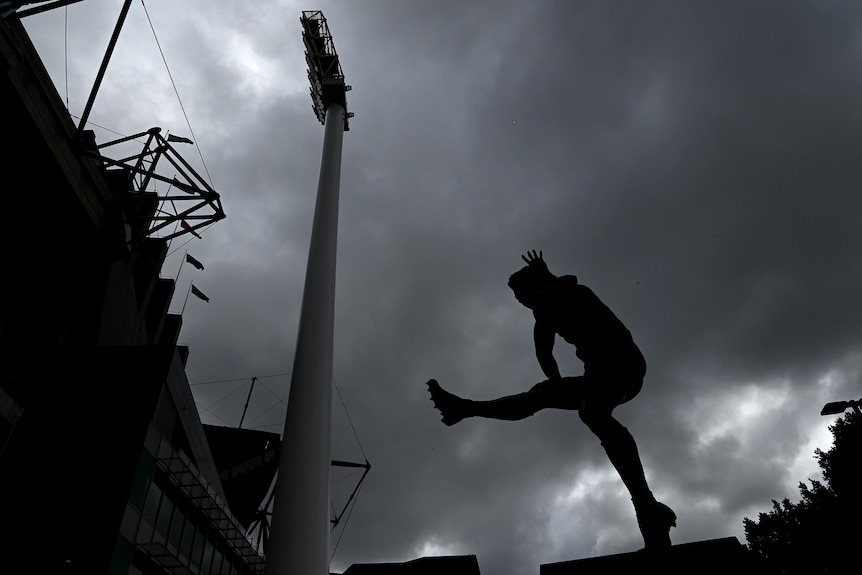 The statue of Ron Barassi is seen outside the MCG with a backdrop of grey, cloudy skies.