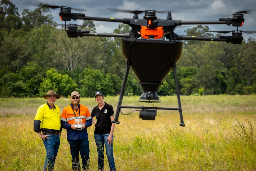 Three people watch as a drone takes off