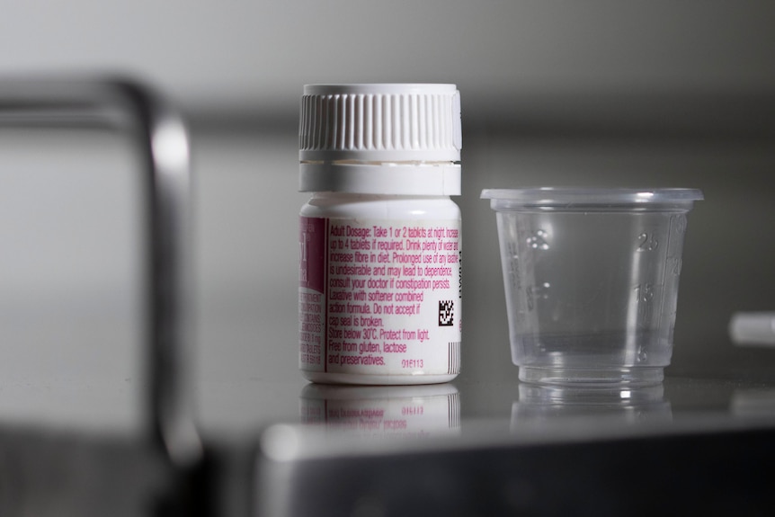 A small medication bottle next to a cup.