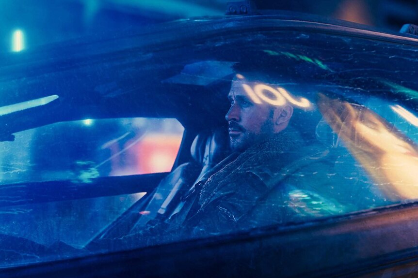 Still image from 2017 film Blade Runner of Ryan Gosling sitting inside a car looking worried.