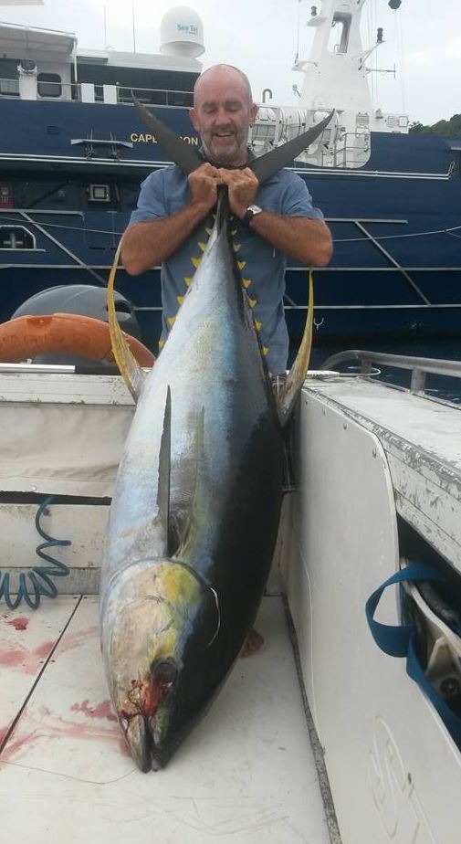 A smiling fisherman in his boat holding a huge tuna by the tail.