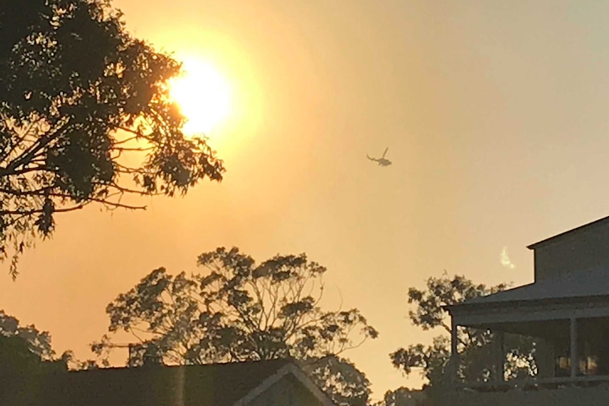 A firefighting helicopter hovers over the Kings Park bushfire in front of the rising sun.